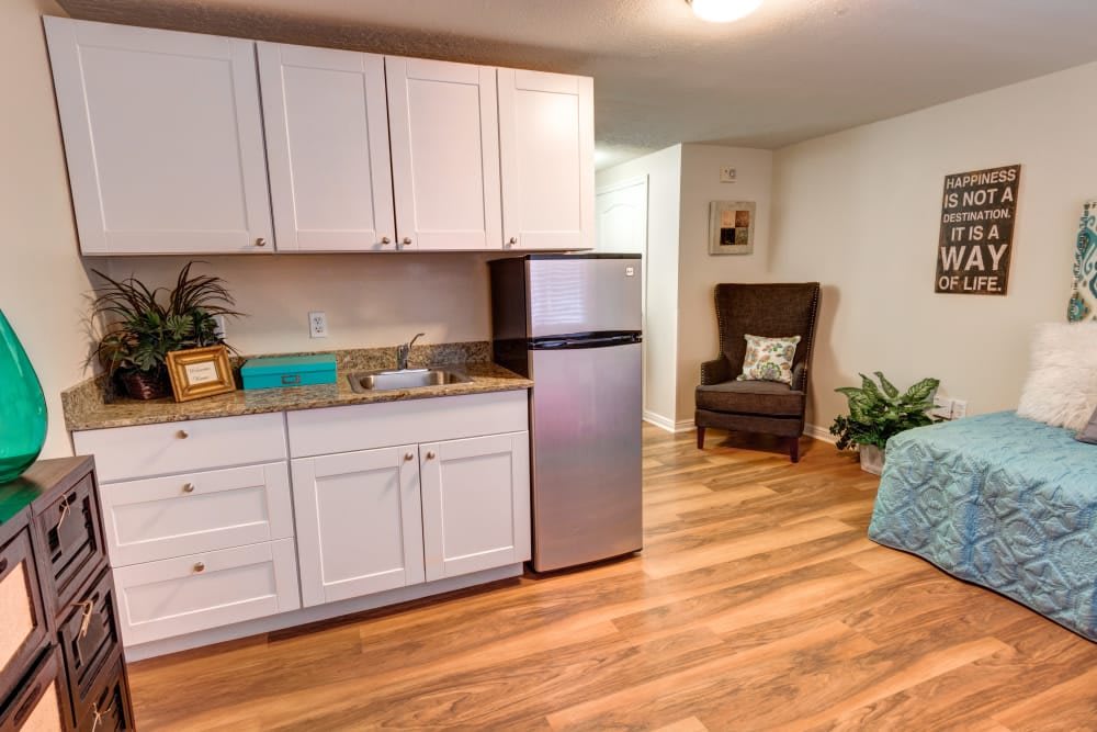 A cozy kitchen area with white cabinets, a stainless steel refrigerator, and wooden flooring.