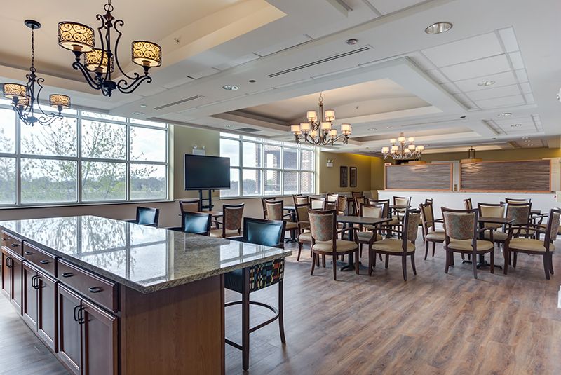A modern dining room with elegant chandeliers, wooden flooring, and neatly arranged tables and chairs.