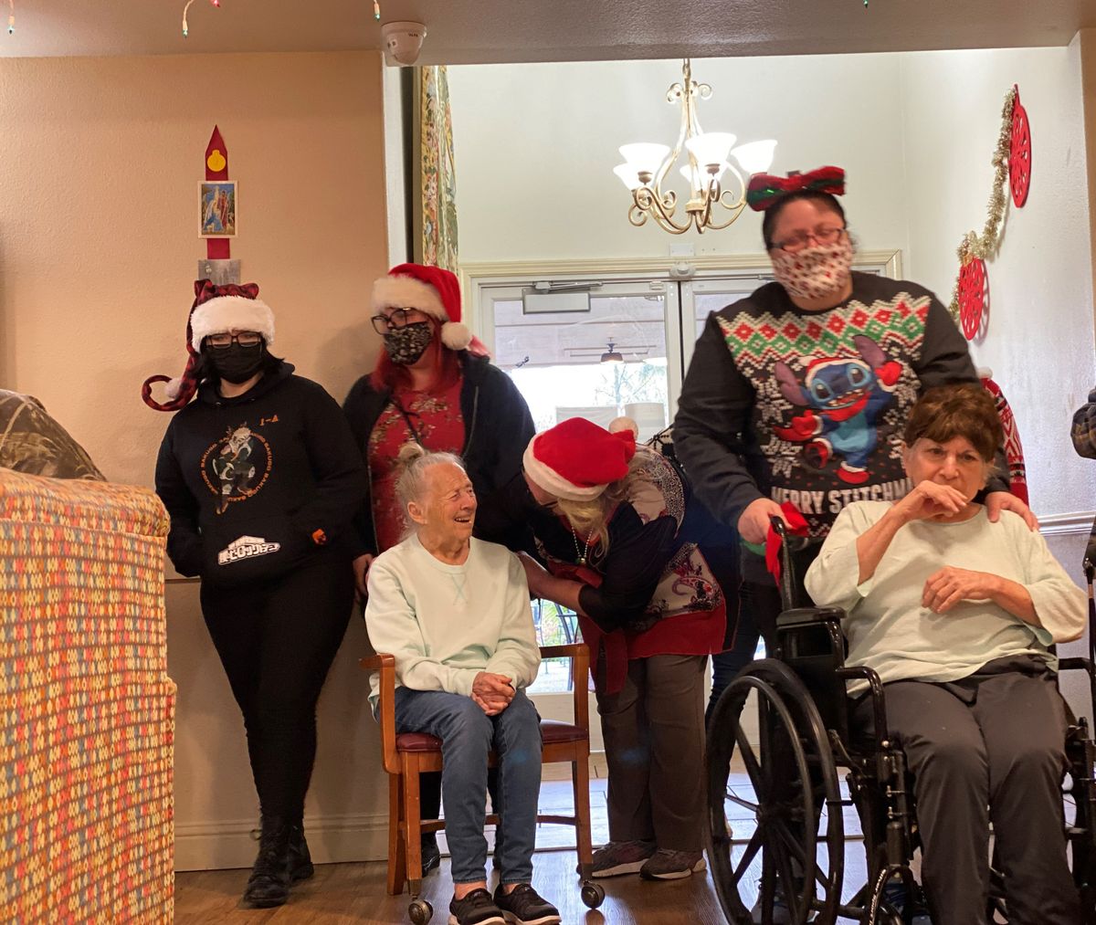 A group of people wearing festive clothing and Santa hats gather indoors for a holiday celebration.