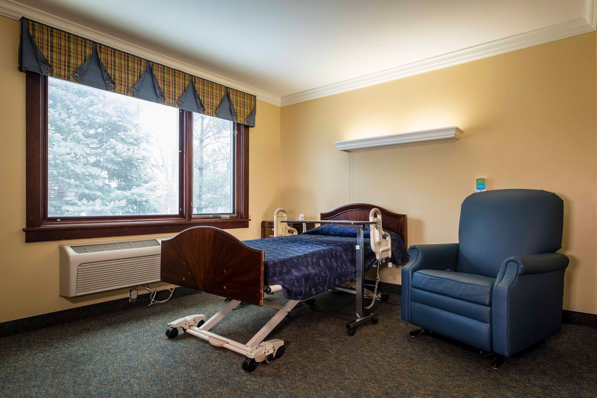 A hospital room with a bed and chair, featuring a window with a view.