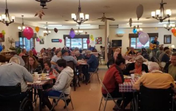 A lively community gathering with people enjoying a meal in a decorated indoor space.