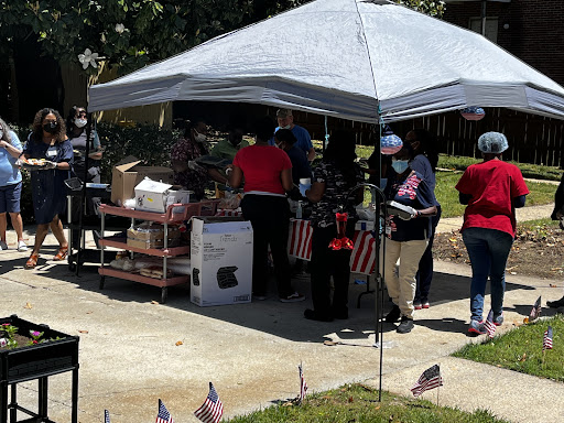 A community gathering under a tent, with people wearing masks and celebrating around American flags.