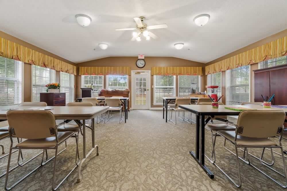 A well-lit community room with multiple tables and chairs arranged in an orderly fashion.