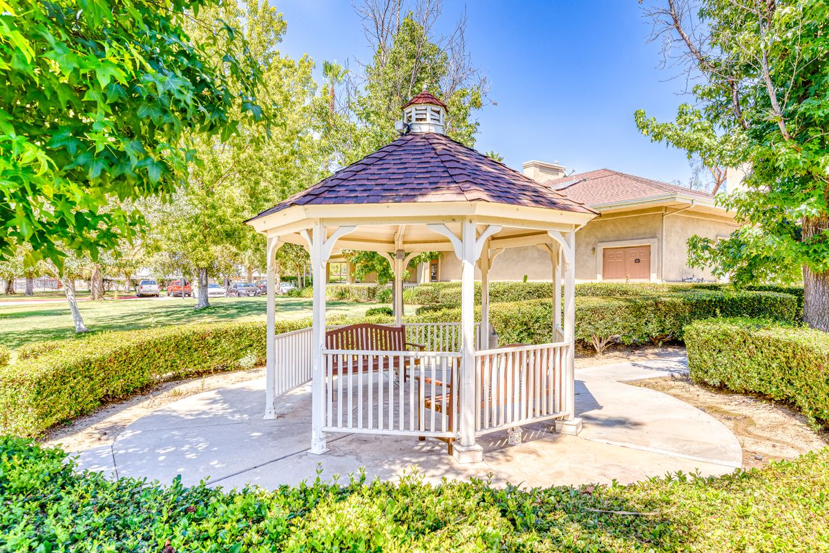 A charming gazebo in a sunny garden setting, surrounded by trees and greenery.