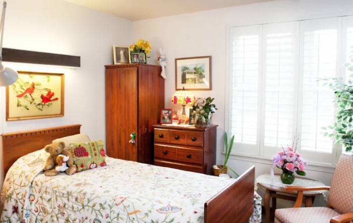 A cozy bedroom with wooden furniture, floral bedding, and various plants adorning the dresser.