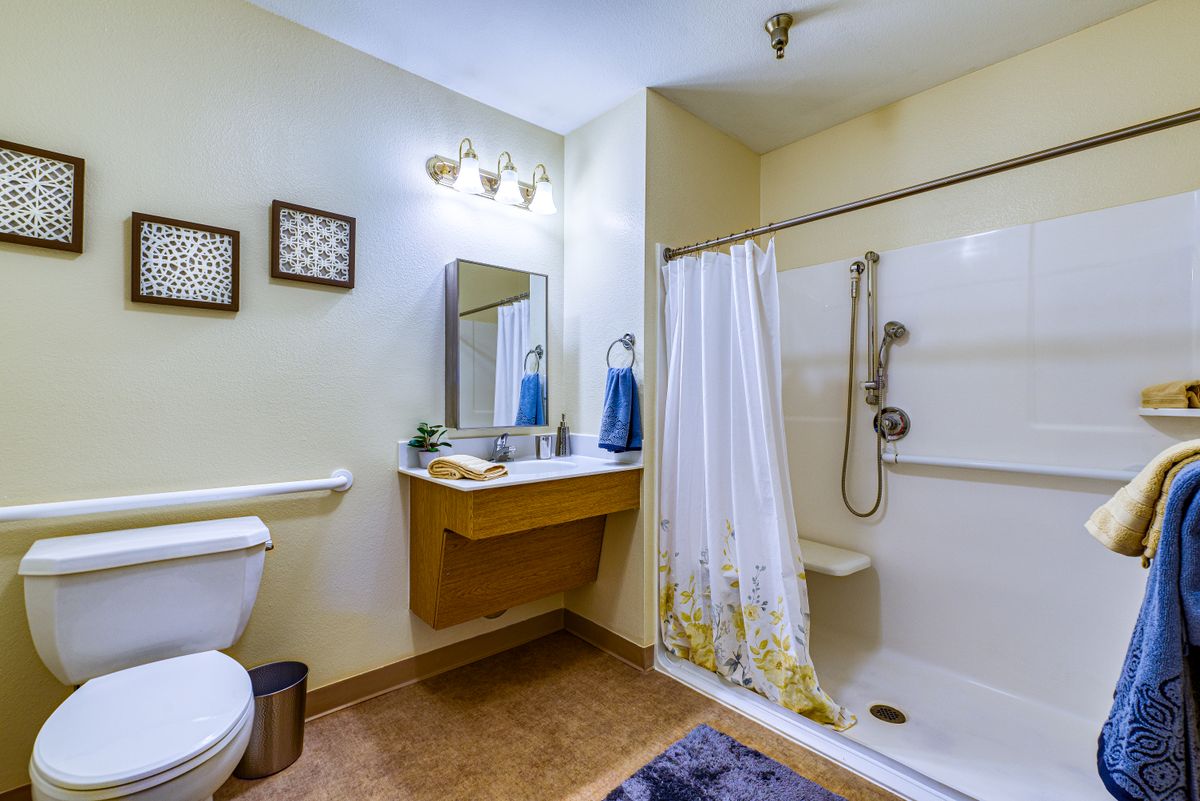 A well-organized bathroom featuring a shower with a curtain, a sink with a mirror, and a toilet.
