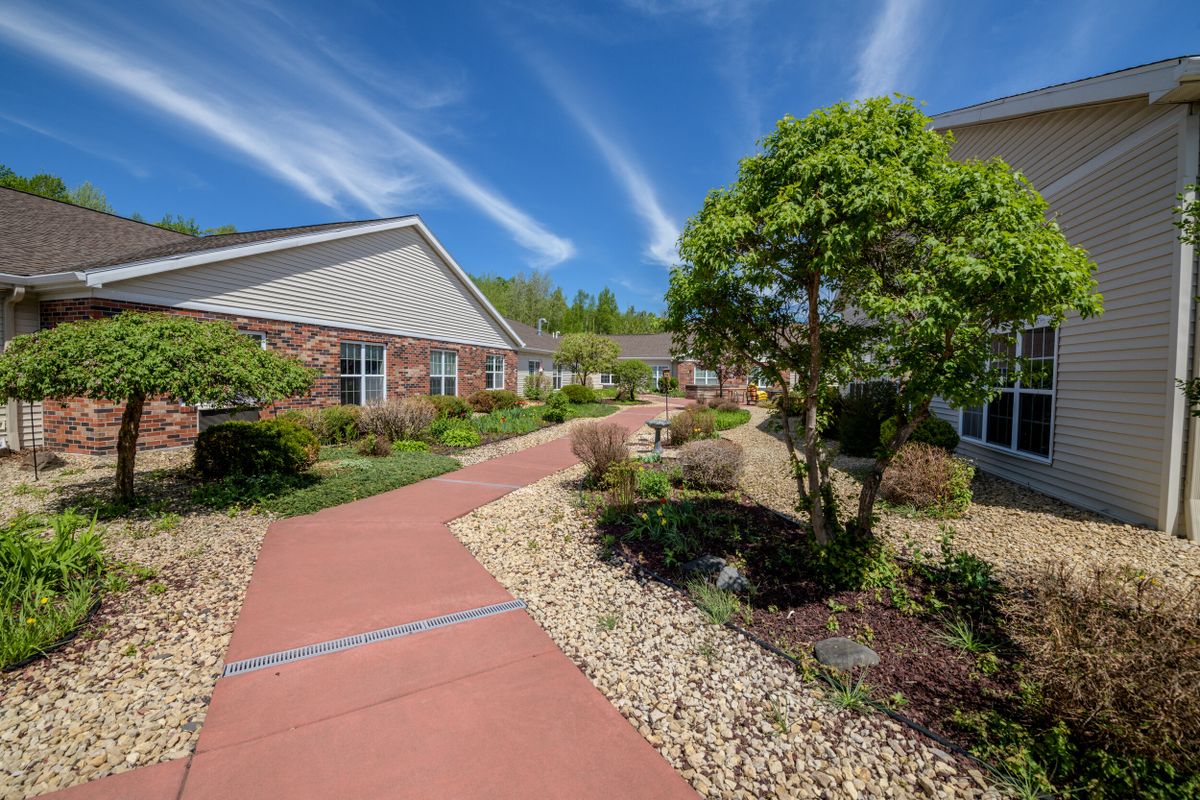 A well-maintained garden with a stone path leading past buildings under a bright blue sky.