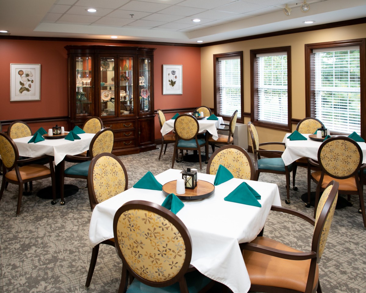 An elegant dining room with neatly arranged tables and chairs, featuring crisp white tablecloths and teal napkins.