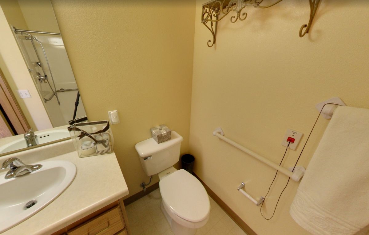A small bathroom featuring a toilet, a sink with a mirror, and a handrail for accessibility.