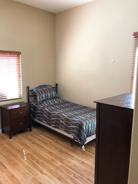 A simple bedroom with a single bed, nightstand, and dresser.