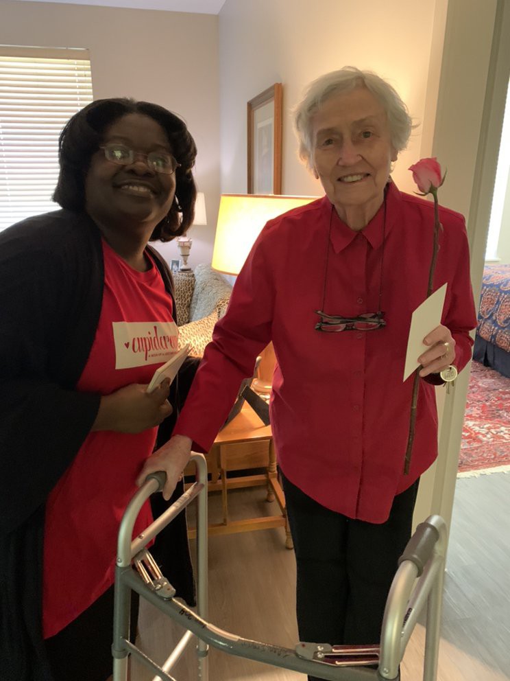 Two people smiling indoors, holding cards and using a walker.
