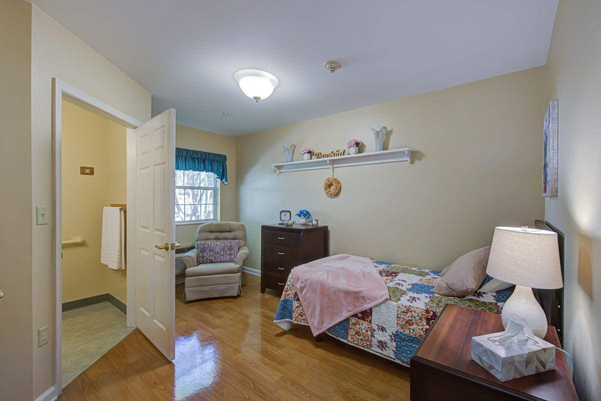 A cozy, well-furnished bedroom with a bed, dresser, and comfortable chair near the window.