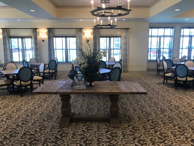 An elegant dining area with a central wooden table, surrounded by chairs, and illuminated by a chandelier.