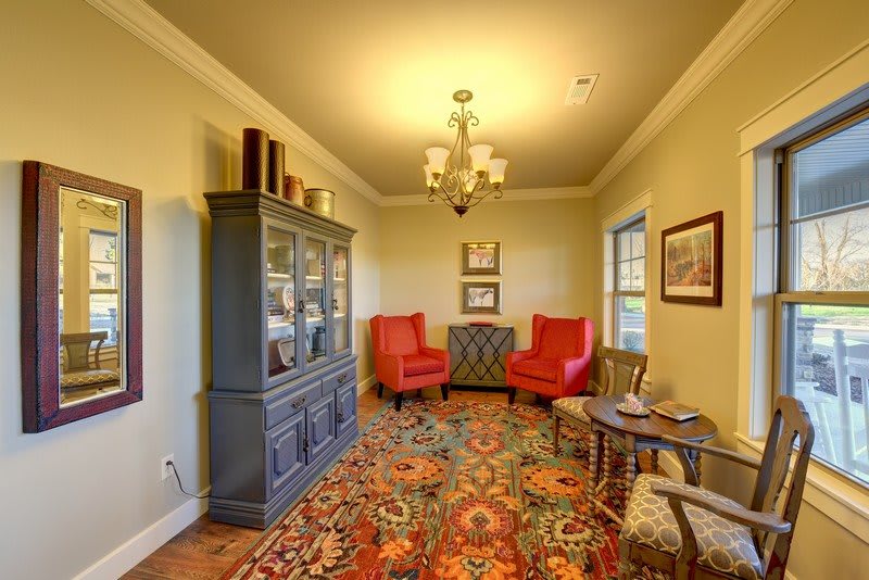 A cozy living room featuring red armchairs, an ornate carpet, and a traditional bookshelf.
