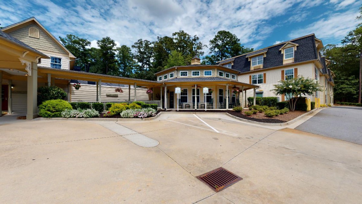 A modern building with a circular entrance and driveway, surrounded by trees and neatly arranged landscaping.