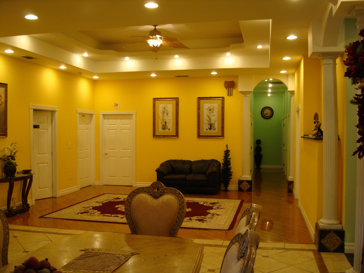 A warmly lit living room with yellow walls, featuring a sofa, artwork on the walls, and a decorative carpet.