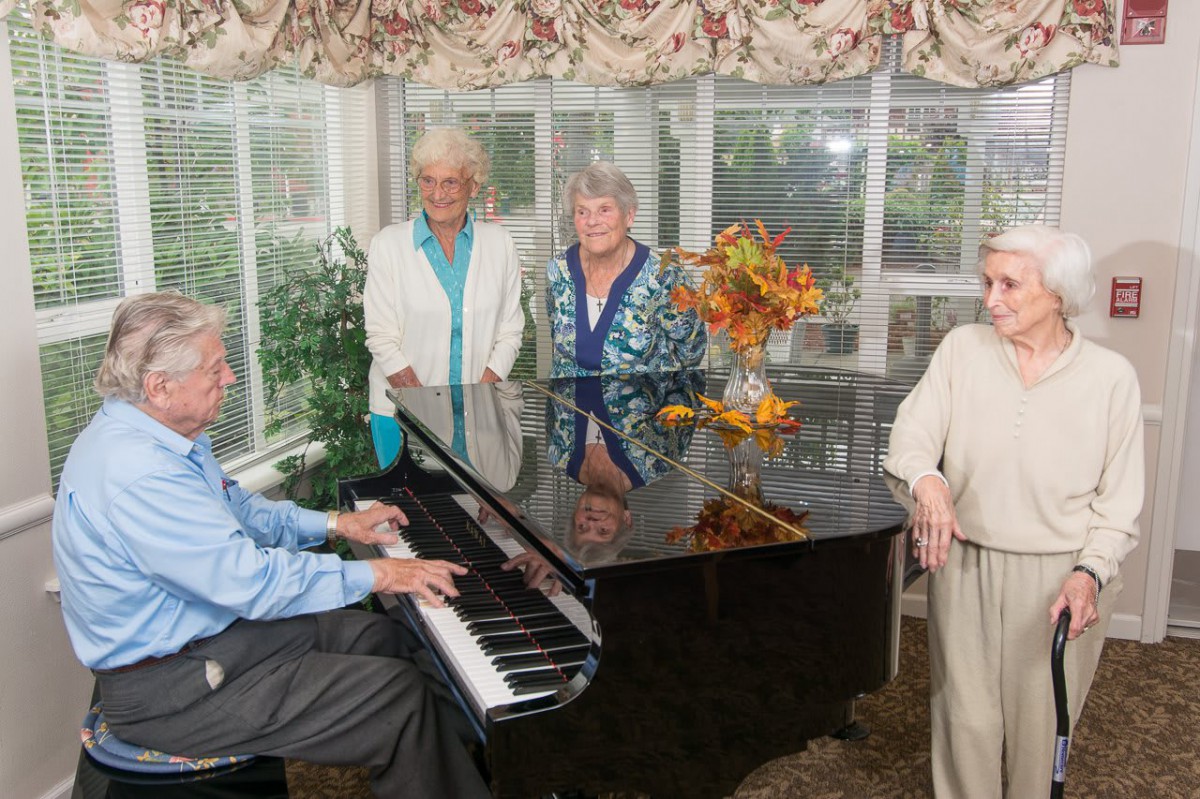 A group of elderly people gathered around a piano, enjoying music indoors.
