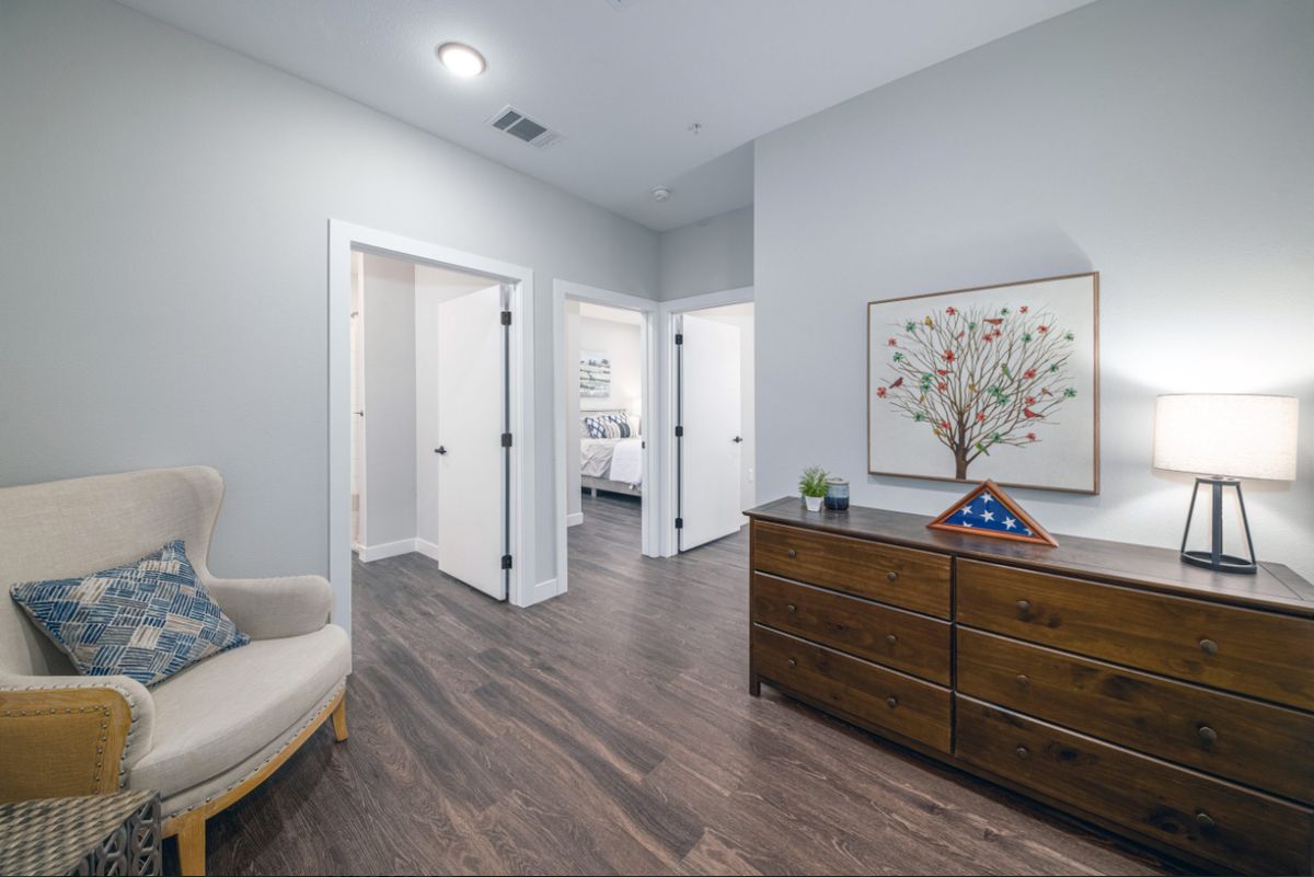A modern hallway with wooden flooring, featuring a dresser decorated with small items and artwork on the wall.