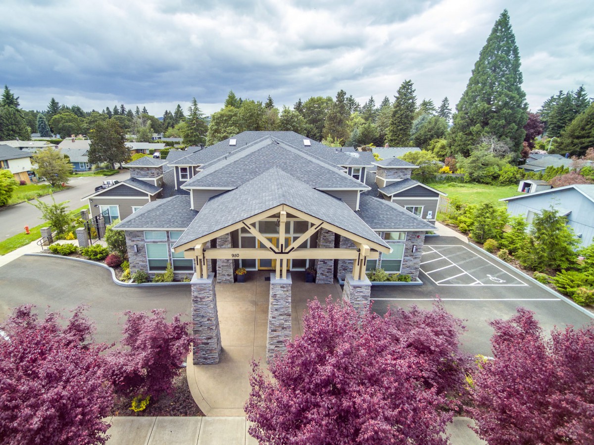 Aerial view of a large building surrounded by trees with a cloudy sky overhead.