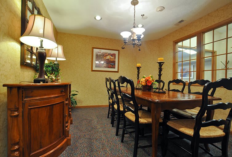 A warmly lit dining room featuring a large wooden table surrounded by chairs, with elegant lighting and decorative elements.