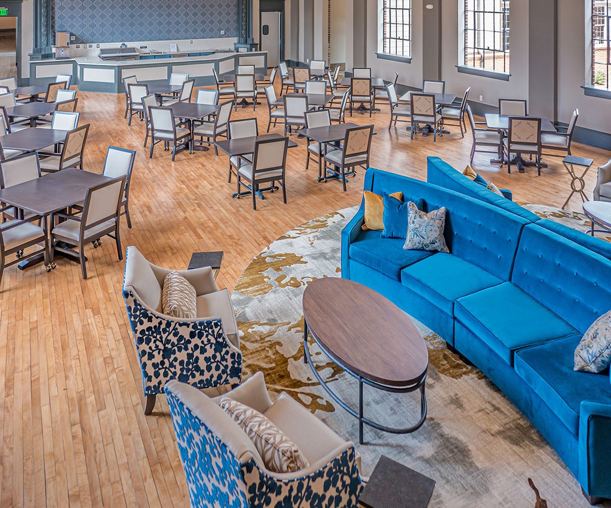 A spacious lounge area with a variety of seating options, including a blue sofa, chairs, and tables on a wooden floor.