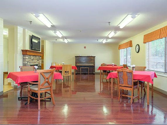A spacious dining area with multiple tables covered in red tablecloths and wooden chairs arranged neatly on a hardwood floor.