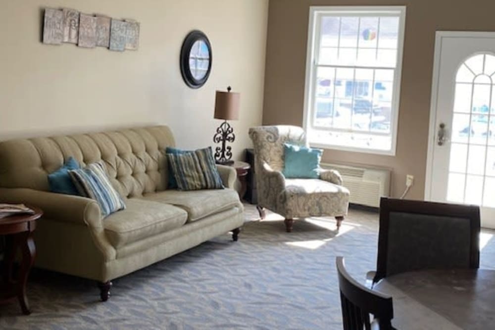 A cozy living room with a sofa, armchair, and large window allowing natural light.