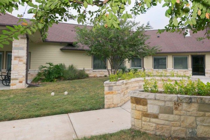 A residential house with a well-maintained yard, featuring trees and shrubs along a stone walkway.