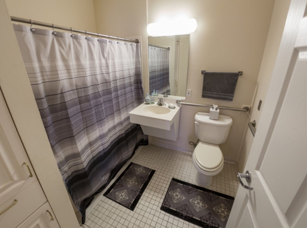 A tidy bathroom with a shower curtain, sink, toilet, and wall-mounted mirror.