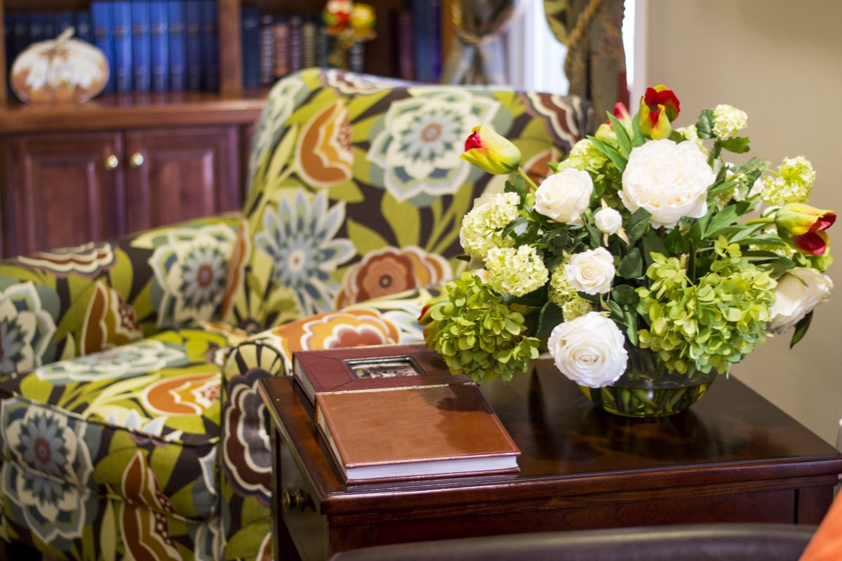 A cozy interior setting featuring a floral-patterned armchair, a small coffee table with books and a bouquet of flowers, creating a warm and inviting atmosphere.