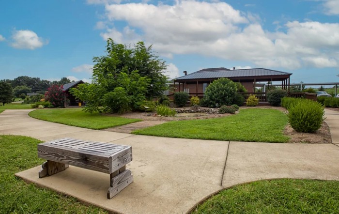 A peaceful residential garden with a bench, lawn, and house under a blue sky.