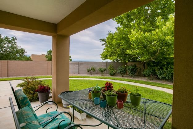 A cozy backyard patio with a metal table and chairs, surrounded by lush greenery and potted plants.