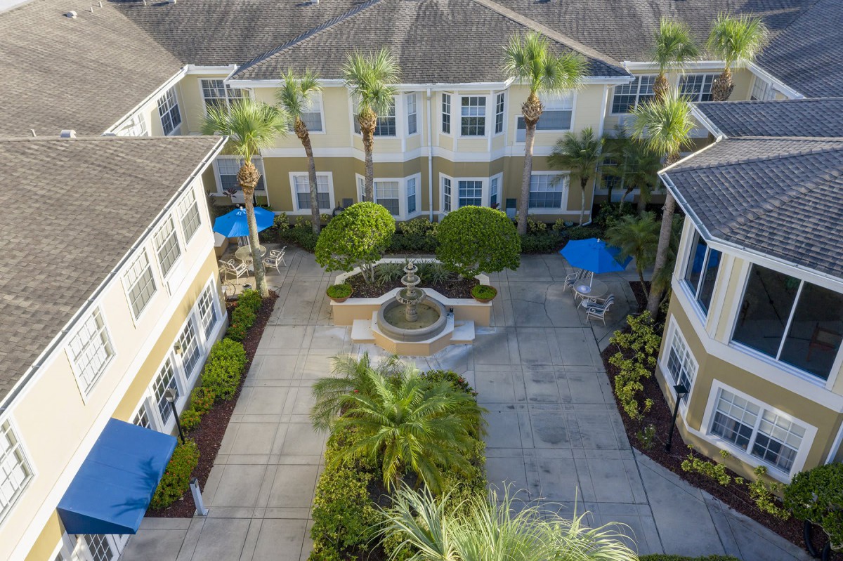 Aerial view of a courtyard with a fountain, surrounded by palm trees and residential buildings.