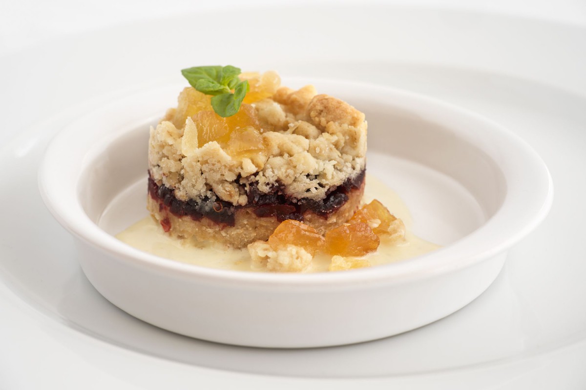 A beautifully plated dessert with a crumble topping and fruit garnish, served on a white plate.