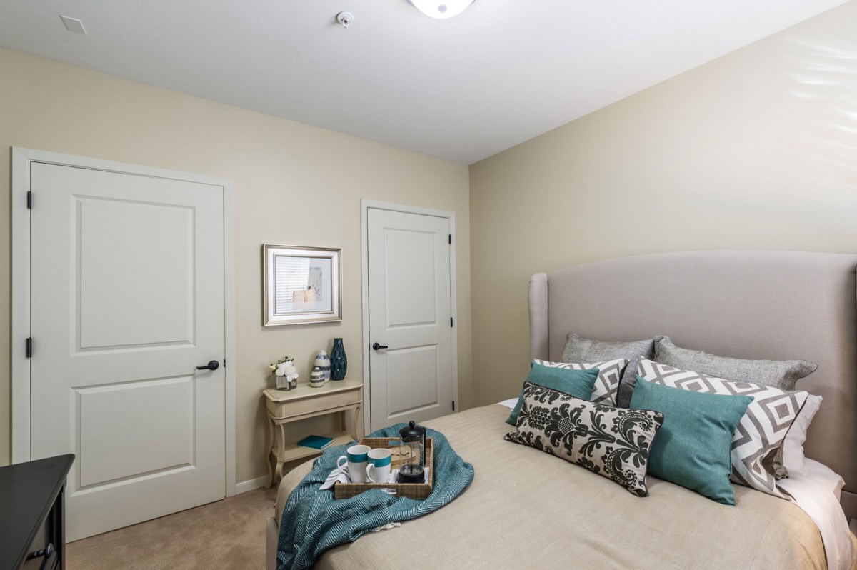 A cozy bedroom with a neatly made bed, featuring decorative pillows and soft lighting, complemented by neutral beige walls.