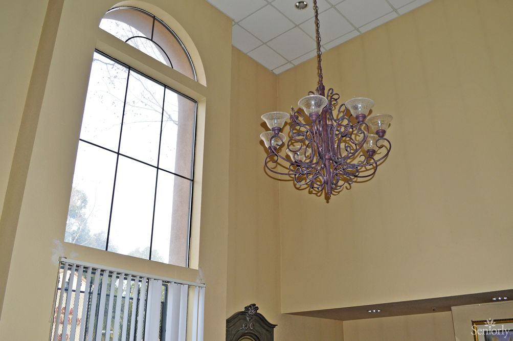 Elegant chandelier hanging in a room with high ceilings and large arched windows.
