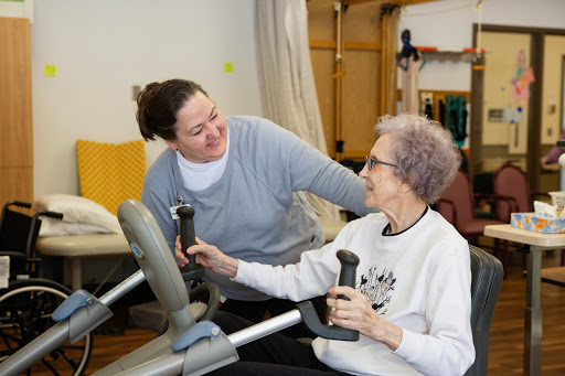 A caregiver assists an elderly woman with her exercise routine using fitness equipment.