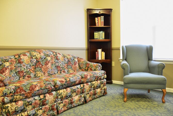 A cozy living room setup with a floral sofa, an armchair, and a bookshelf filled with books.