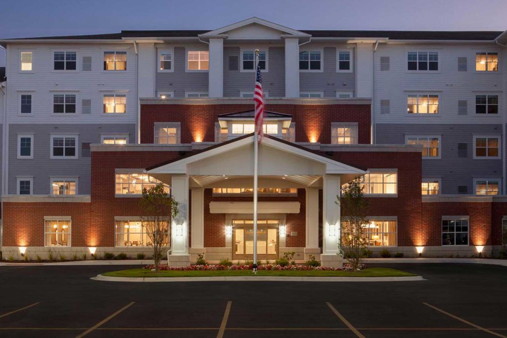 A well-lit building entrance at night, featuring an American flag and classic architectural design.