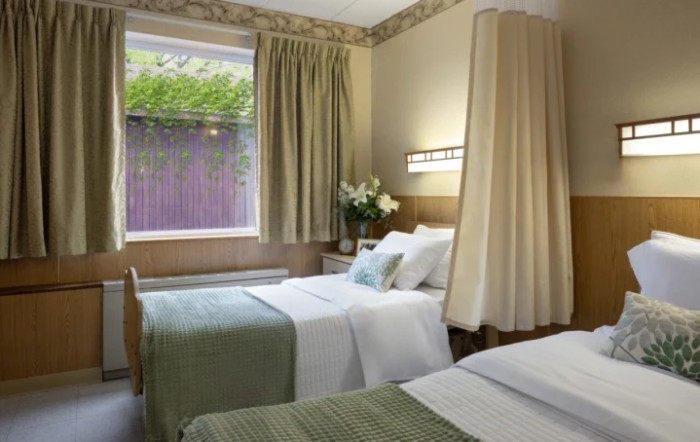 A cozy hotel room with two neatly made twin beds, complemented by elegant curtains and a view through the window.