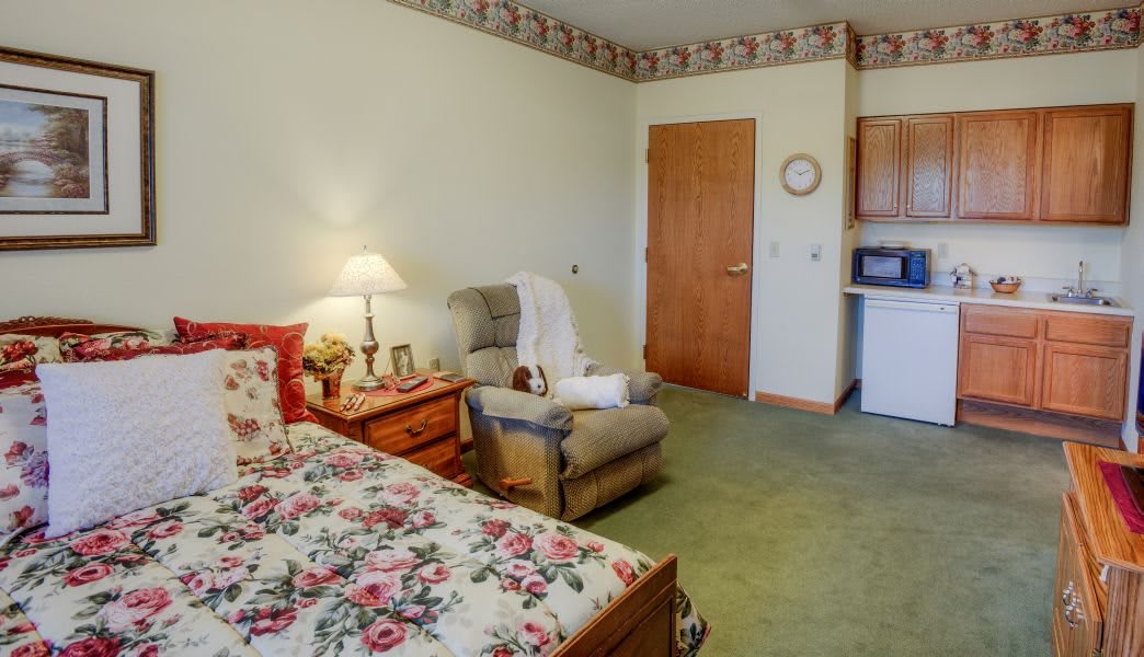 A cozy bedroom with floral bedding, a comfortable chair, and warm lighting.