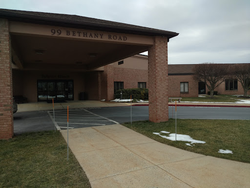 The entrance to a building on a cloudy day, featuring a sidewalk and parking area.
