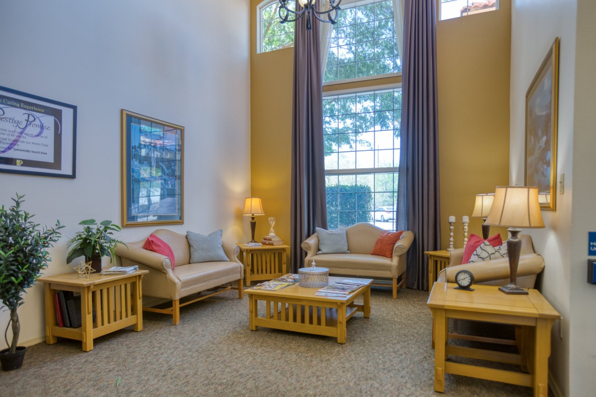 A cozy living room with high ceilings, featuring comfortable sofas, a coffee table, and large windows adorned with curtains.