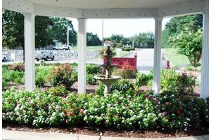 A beautiful garden view from inside a gazebo, featuring a fountain surrounded by lush flowers and greenery.