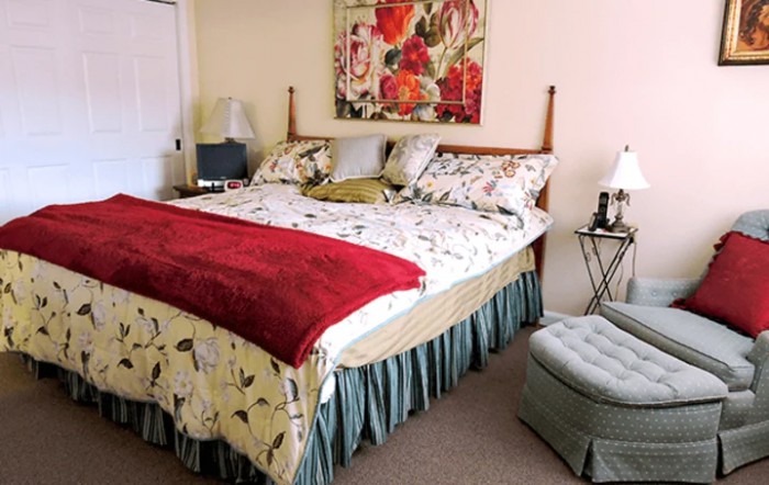 A cozy bedroom with a floral bedspread and vibrant red throw blanket.