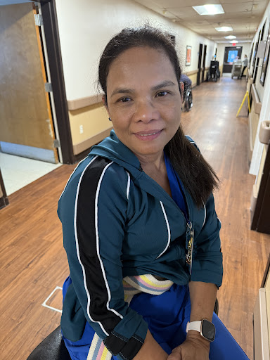 A woman in casual attire smiles while sitting in a healthcare facility.