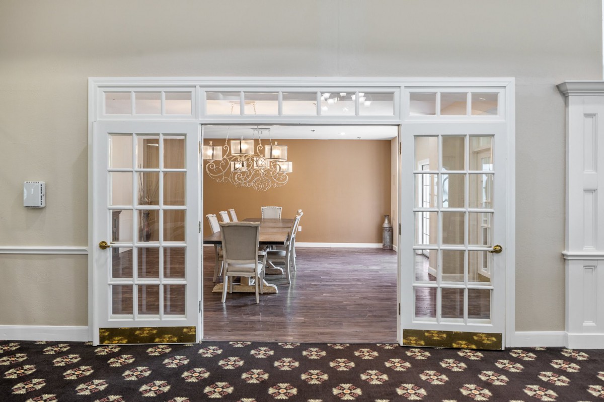 A classic dining room with a chandelier, viewed through elegant glass doors.