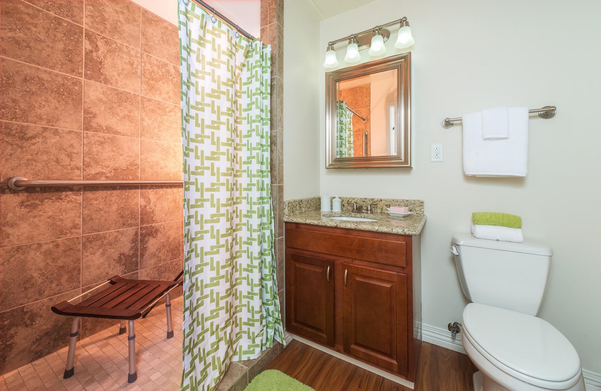 A bathroom with a shower featuring a curtain, wooden cabinet under the sink, and a toilet.