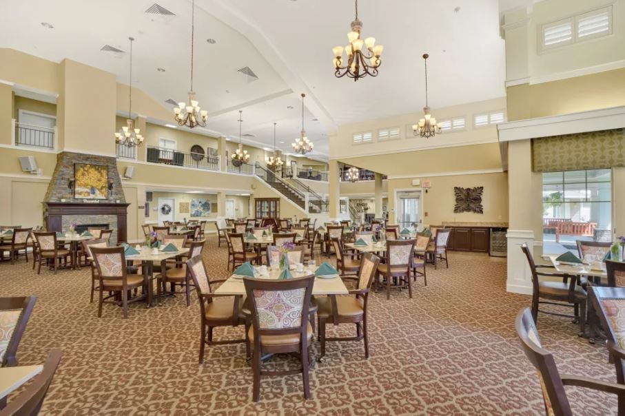 A spacious and elegantly decorated dining area with multiple tables, chandeliers, and bright lighting.