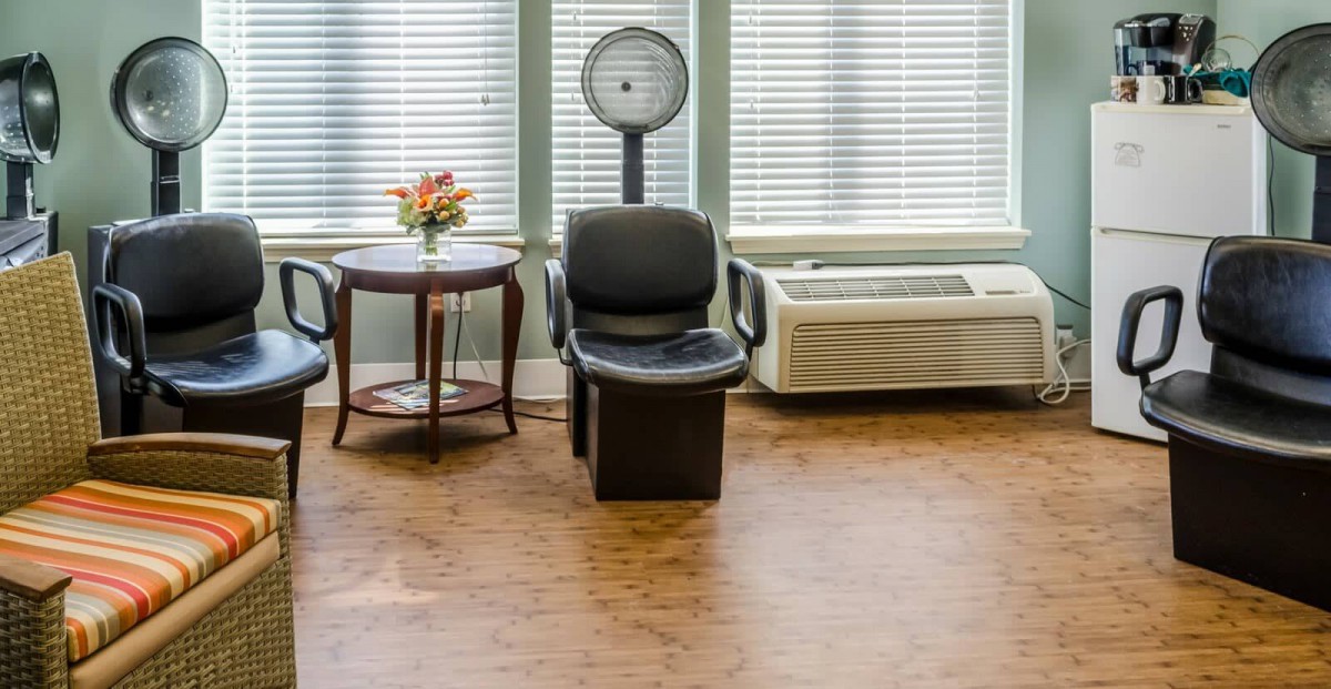 A salon waiting area with a hair dryer chair and a small table holding a flower vase.